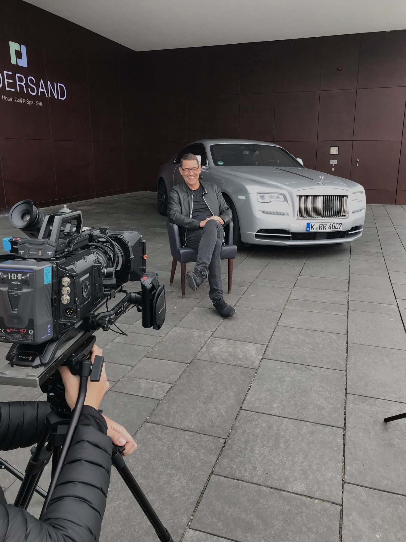 Interview vor einem silbernen Rolls-Royce in einer Showroom-Halle, Kamera im Vordergrund