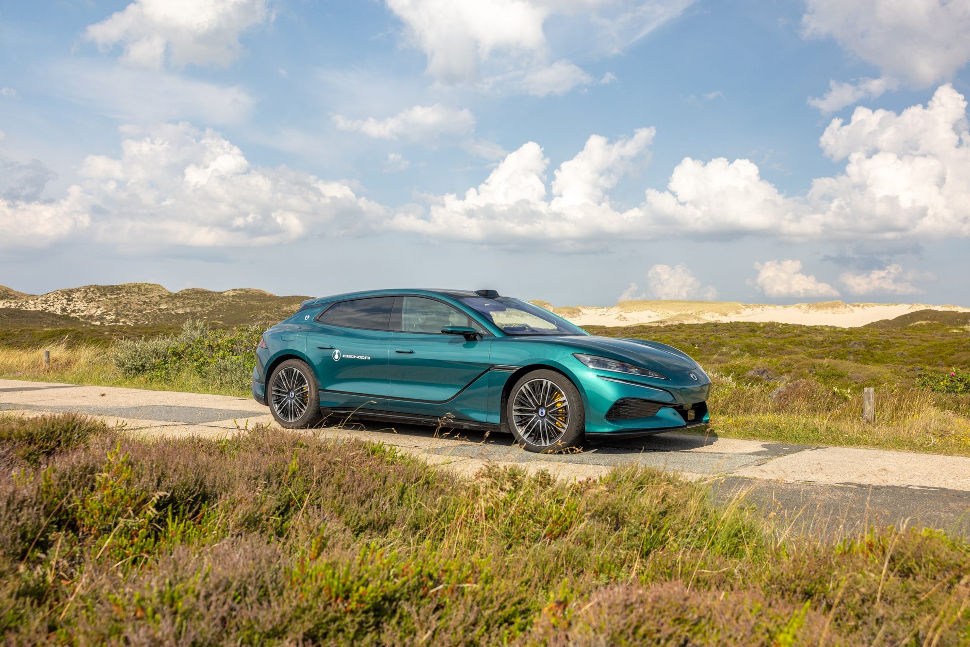 DENZA Z9GT in Petrol auf einem Weg durch die Heide, im Hintergrund Dünen
