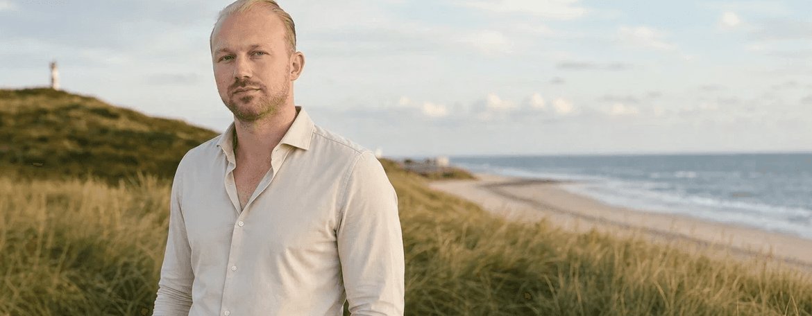 Michael Hoppe im hellen Hemd in den Dünen, dahinter Strand und Nordsee
