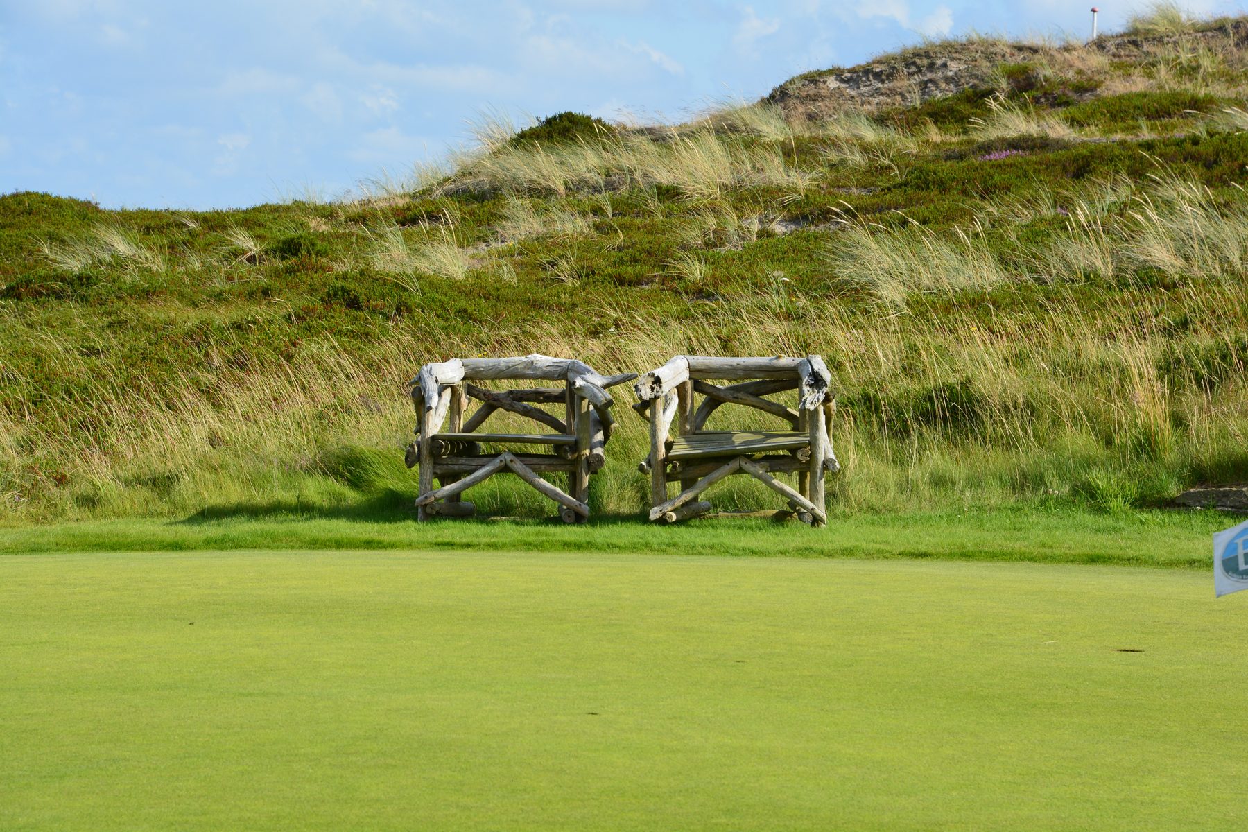 Zwei Holzstrandkörbe am Rand eines Golfplatzes vor Dünen