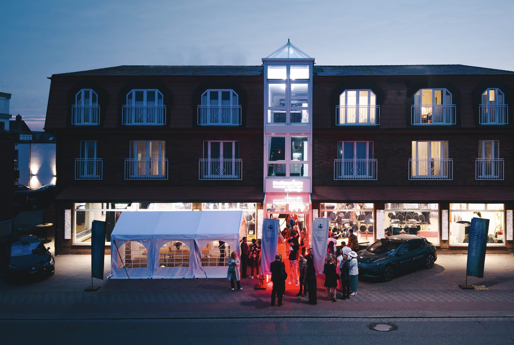 Fassade des Concept Stores in Westerland am Abend, Pavillon und Gäste vor dem Eingang