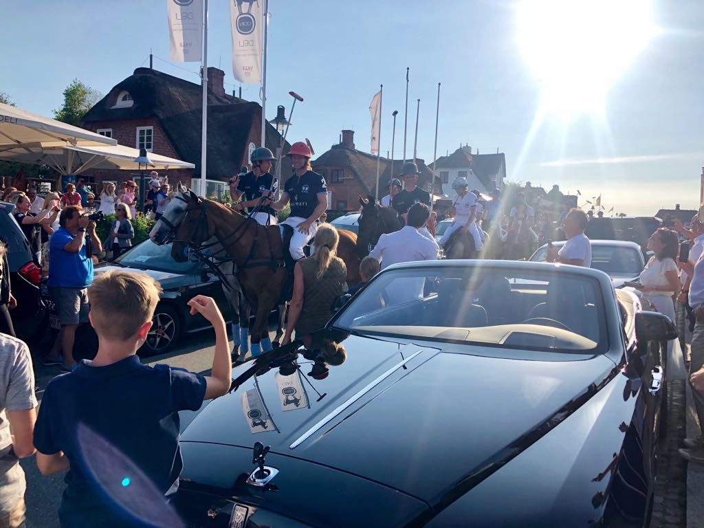 Menschenmenge bei einem Polo-Event, im Vordergrund ein dunkles Cabrio im Gegenlicht