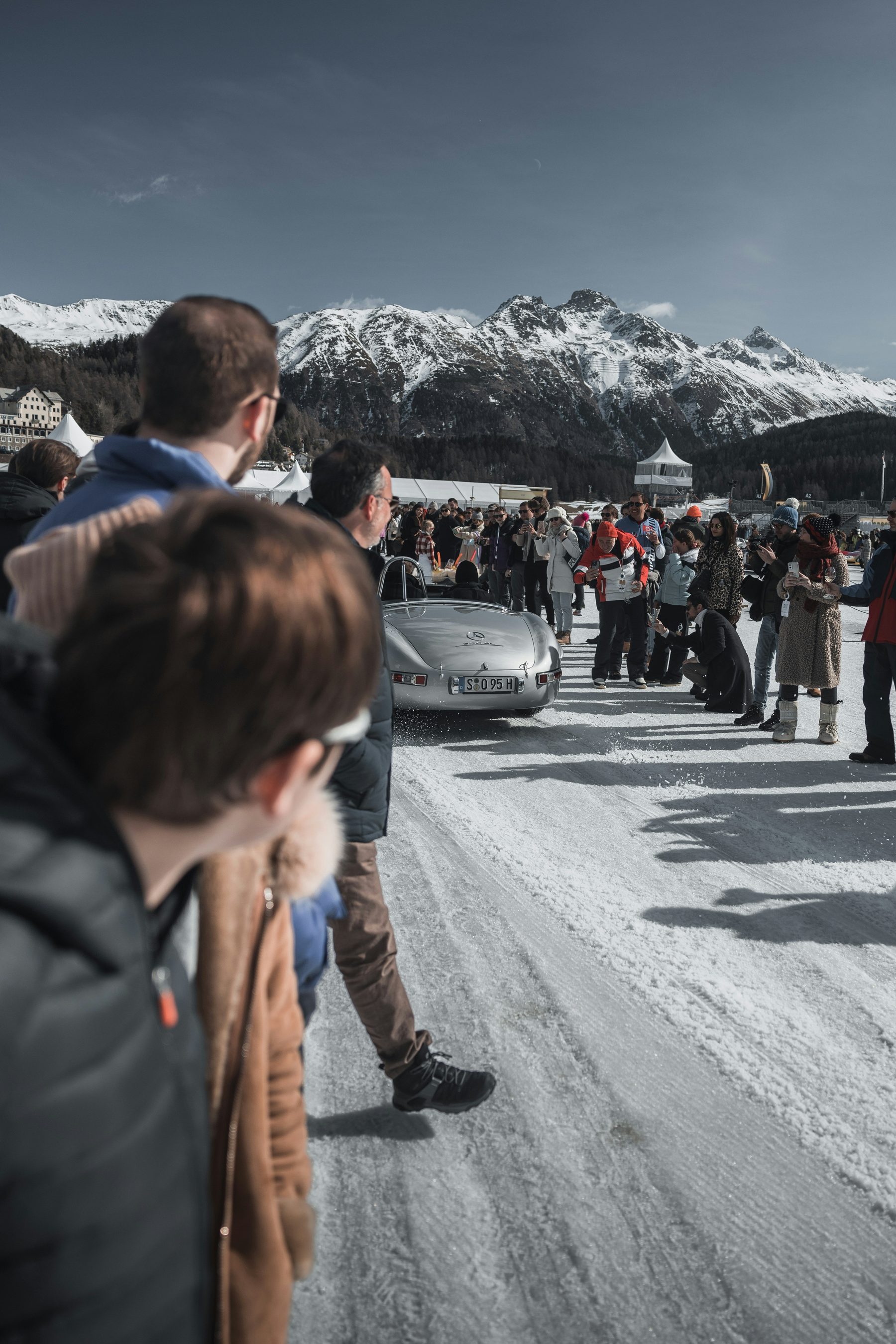 Gäste neben einem Oldtimer auf schneebedeckter Straße vor Bergen