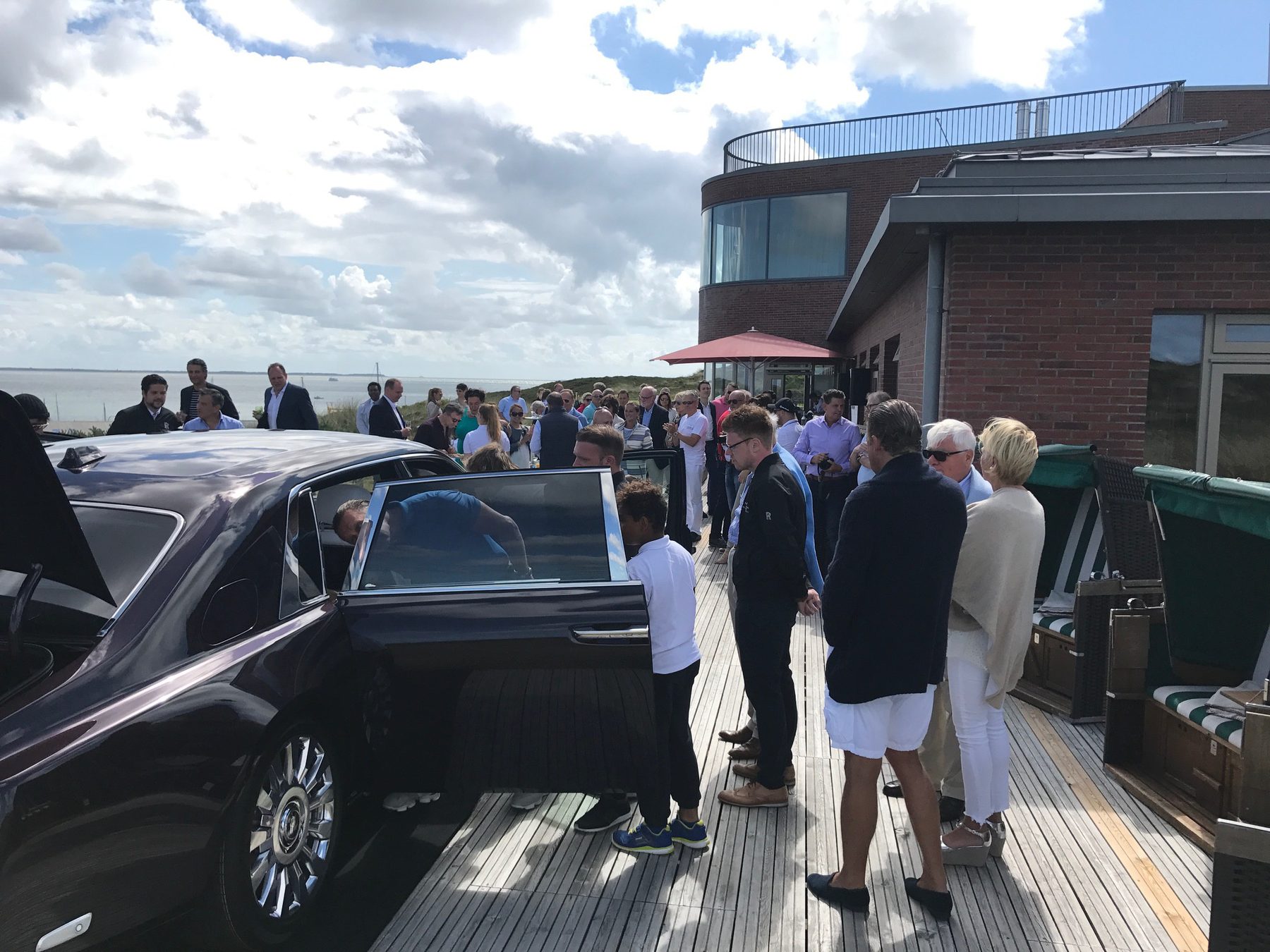 Gäste steigen auf einer Terrasse am Meer aus einer schwarzen Limousine